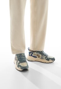 Baskets de sport avec un motif camouflage comprenant des nuances de bleu, beige et marron. Tige en tissu, accents texturés et semelle épaisse.