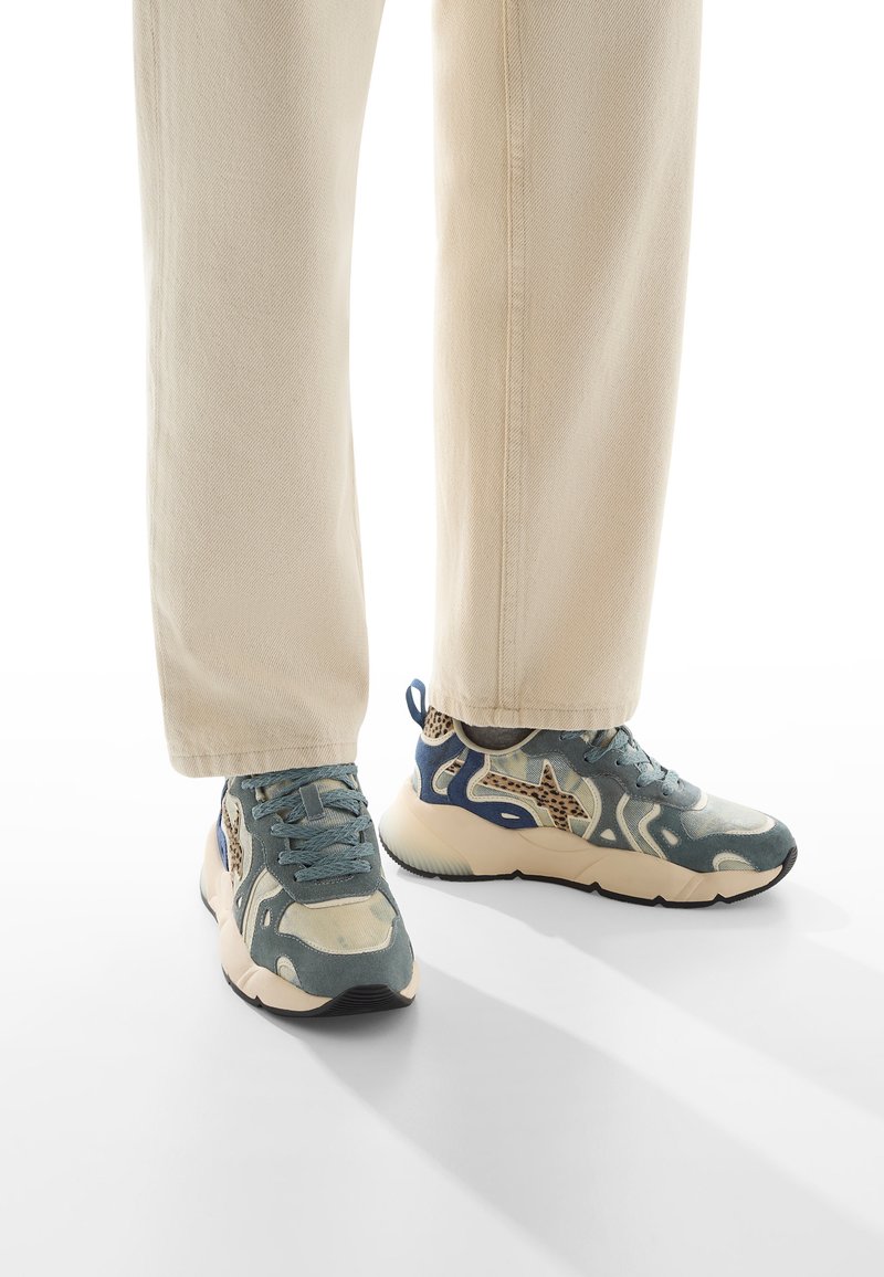 Baskets de sport avec un motif camouflage comprenant des nuances de bleu, beige et marron. Tige en tissu, accents texturés et semelle épaisse.