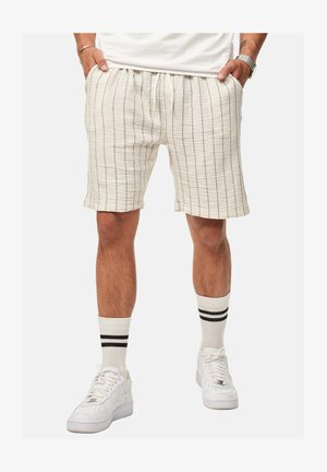Light beige shorts with vertical stripes, elastic waistband, and pockets. Paired with white sneakers and striped white socks.