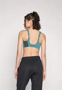 Sport bh i teal med svarte striper, justerbare stropper og en krok-og-løkke lukking. Glatt stoff og en minimalistisk design. Parret med sorte bukser.