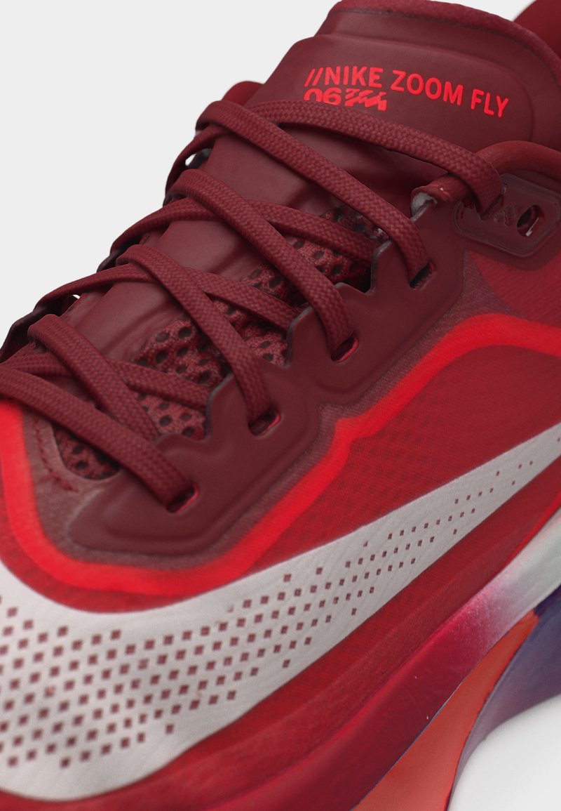 Zbliżenie na czerwony but do biegania Nike Zoom Fly z detalicznymi sznurowadłami, siateczkową cholewką oraz jaskrawobiałym logo Nike po boku.