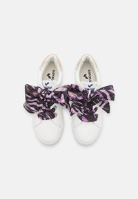 Sneakers bianchi con una finitura testurizzata e grandi fiocchi in tessuto nero e viola a fantasia. Presentano un'etichetta con il logo sulla linguetta e dettagli in contrasto.
