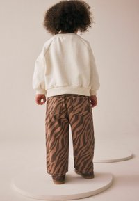 Kremowa bluza z teksturowanej tkaniny i ściągaczami, w zestawie z brązowymi spodniami typu wide-leg w tygrysie paski, z tylnymi kieszeniami.