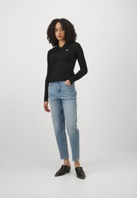 Camisa polo negra de manga larga con costillas y un pequeño logo, combinada con jeans rectos de pierna recta azul claro y mules de tacón negros y sin cordones.