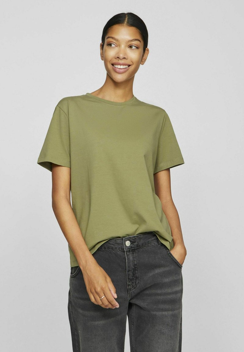 Olivgrön bomullströja med korta ärmar, rund hals och avslappnad passform. Kombinerad med mörkgrå denimjeans.