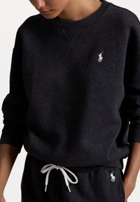 Tmavě šedá mikina vyrobená z měkkého materiálu, s bílým logem polo na hrudi, s ribbed manžetami a bílou stahovací šňůrkou v pase.