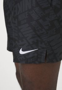 Pantaloni scurți atletici negri cu un model repetat al logo-ului Nike și un swoosh alb Nike pe lateral, având un tiv despicat pentru mobilitate.