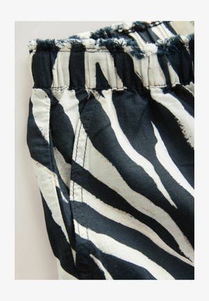 Tkanina sa uzorkom crno-bijelih zebri, sa naboranim pojasom, koja sadrži rasparani rub i vidljive šavove na bočnom šavu.
