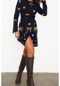 Strick-Outfit mit einem marineblauen Bodycon-Kleid, das Palmbaum- und geometrische Muster aufweist, kombiniert mit braunen kniehohen Stiefeln mit Absatz.