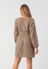 Abito lavorato a maglia beige con un motivo testurizzato, maniche a palloncino e una vita adatta. Cade a metà coscia con una silhouette casual.