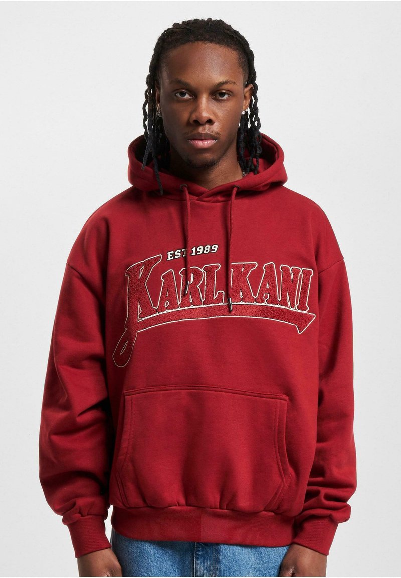 Rød hettegenser med "KARL KANI"-logo, frontlomme og ribbestrikkede mansjetter og kant. Laget av mykt, teksturert stoff.