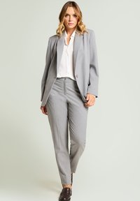 Blazer y pantalones grises a medida con un sutil patrón de puntos; blusa blanca lisa debajo; combinados con zapatos marrón oscuro; textura de tela suave.