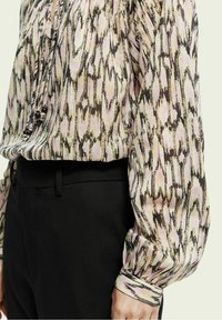 Blusa a fantasia in rosa chiaro e marrone con maniche fluide, caratterizzata da un tessuto texture e dettagli arricciati sullo scollo.