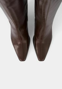 Brązowe, skórzane kozaki za kolano z szpiczastym noskiem, o gładkiej fakturze i subtelnych szwach. Podeszwa w kolorze czarnym.