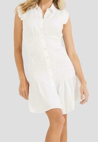 Weißes ärmelloses Kleid mit Knopfleiste, gerafftem Mittelteil und ausgestelltem Rock. Es verfügt über geraffte Schulterdetails und eine weiche Textur.