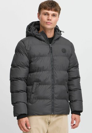 Grey puffer jacket with a hood, featuring horizontal stitching, logo patch on the chest, and zippered front closure. Textured, warm fabric.