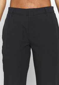 Svarta byxor med en slät yta och en skräddarsydd passform, med rak ben, bälteshällor och en dold framdragkedja.