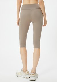 Leggings capri ajustados de color beige con una cinturilla ancha. Textura suave, longitud a media pantorrilla. Llevados con zapatillas deportivas de color claro.