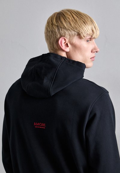 Hanorac negru cu nervuri, dotat cu glugă și șnur, având broderie roșie "AMORE EMPORIO ARMANI" pe spate. Textură moale, design casual.