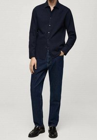 Camicia button-up blu navy scuro, maniche lunghe, abbinata a jeans dritti blu scuro. Scarpe nere completano l'outfit. Tessuto e vestibilità casual.