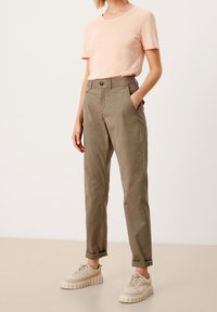Top rosa chiaro a maniche corte abbinato a pantaloni verdi oliva a gamba affusolata con tasche. Calzature: sneakers beige con suola testurizzata.