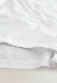 Soutien-gorge blanc avec une couche supérieure lisse et satinée et une sous-couche texturée en dentelle, doté de coutures douces et d'un ajustement confortable.