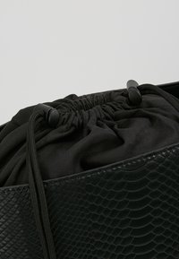 Sac à main en texture de serpent noir avec un haut rond et froncé en tissu noir, doté de fermetures à cordon réglables et d'accents en cuir lisse.