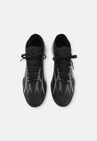 Un par de zapatillas deportivas negras con patrones en zigzag grises, cordones negros y suelas blancas, mostradas desde una vista superior sobre un fondo blanco.