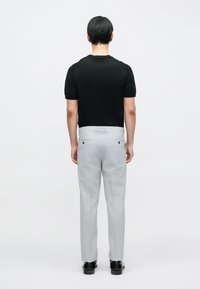 Juoda trumpomis rankovėmis marškinėliai, derinami su šviesiai pilkomis kelnėmis, kurios turi tiesias kojas ir du galines kišenes su juodais mygtukais.