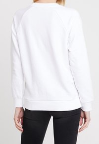 Felpa bianca con scollo rotondo, polsini e orlo inferiore a costine, caratterizzata da una superficie liscia e design delle maniche a raglan.