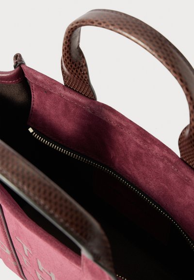 Bordeaux ruskinds håndtaske med brune teksturerede læderhåndtag og en åben top, der viser en lynlåslomme indeni.