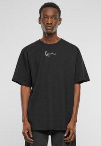 Black cotton T-shirt with a relaxed fit, featuring a white signature design on the chest and short sleeves. Simple, unadorned style.