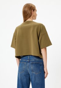 Olijfgroene cropped top met korte mouwen en geribde textuur; gecombineerd met hooggesneden blauwe spijkerbroek met achterzakken.
