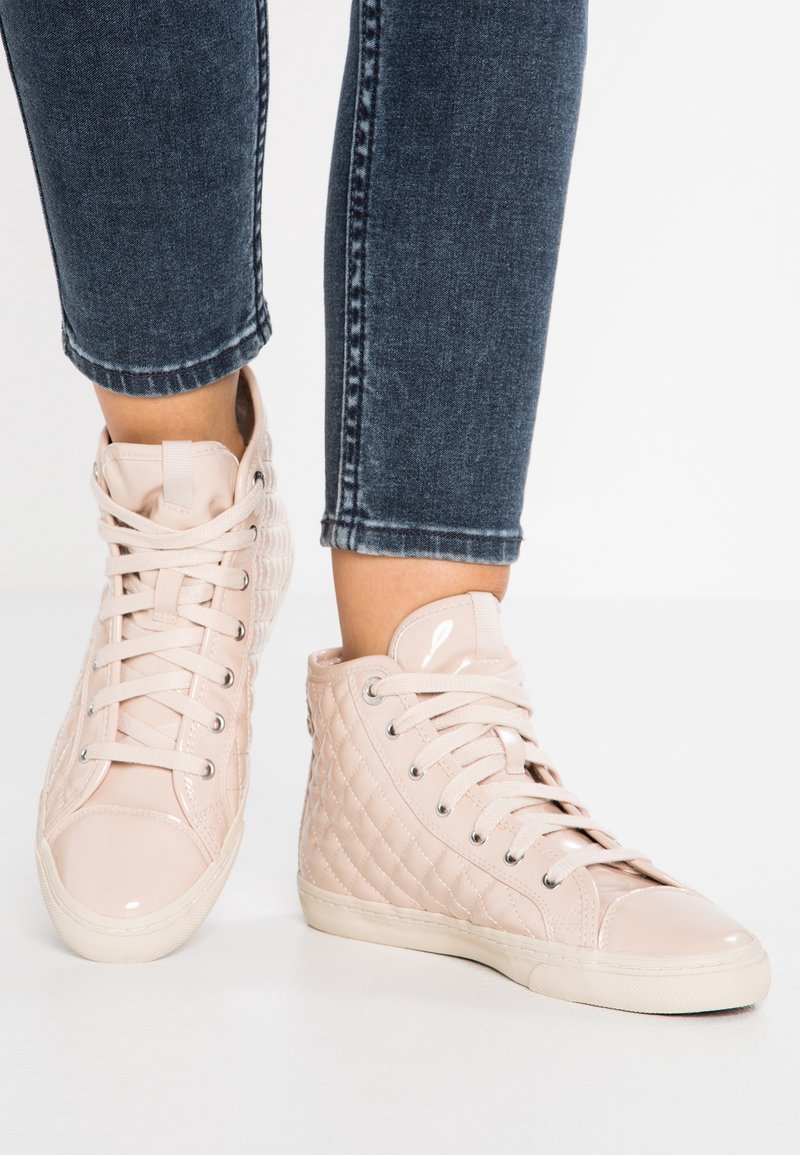Ljusrosa höga sneakers med quilteffekt, glansiga detaljer och platta snören. Kombinerade med mörka jeans.