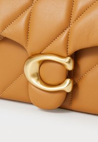 Quilted tan leather handbag featuring a gold metal clasp. Surface has a smooth texture with visible stitching and rounded accents.