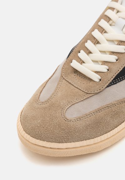 Baskets en daim marron clair avec accents beige. Présentent une surface texturée, un embout rond et des lacets crème. Semelle en caoutchouc avec des rainures.