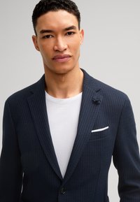 Marine gestreepte blazer van gestructureerde stof, met een enkele knoop, notch revers en een witte zakdoek op een wit T-shirt.