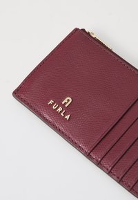 Burgunderfarbene Ledergeldbörse mit strukturierter Oberfläche, ausgestattet mit mehreren Kartenfächern und einem goldenen "FURLA"-Logo. Sichtbares Reißverschlussdetail.