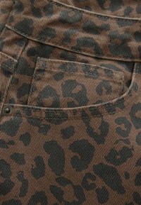 Gros plan sur un tissu en denim marron avec imprimé léopard noir et poche cousue avec rivet métallique sur un vêtement.