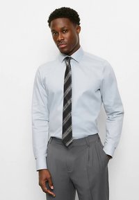 Light blue long-sleeve dress shirt with a collar, paired with a black tie featuring white stripes, and gray pleated dress pants.