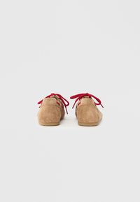 Cipele od brušene kože u bež boji s crvenim vezicama, niskog profila i zaobljenog vrha. Glatka tekstura i minimalistički silueta.