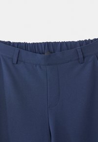Marineblauwe broek met elastische tailleband, riemlussen en verborgen sluiting aan de voorkant, weergegeven van de taille naar beneden op een witte achtergrond.