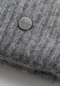 Grijze gebreide stof met een zachte textuur, voorzien van een ronde metalen knop met de opdruk "PEARL WOOD." Gedetailleerd ribbelontwerp.