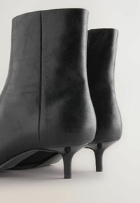 Juodi odiniai kulkšniniai batai su elegantišku dizainu, siauru siluetu ir plonu stiletu kulnu. Matoma lygi tekstūra ir minimalūs siūlių detalės.
