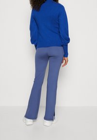 Kungligt blå långärmad topp med puffärmar kombinerad med ljusblå utsvängda byxor. Outfiten har en mjuk textur och en avslappnad passform.