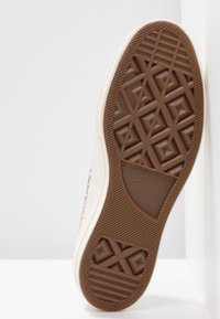 Semelle en caoutchouc d'une basket Converse All Star marron avec des motifs géométriques, semelle intermédiaire blanche et marquage de taille 41.