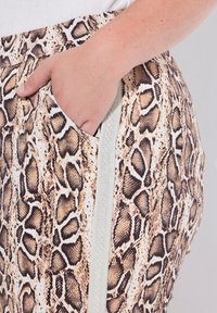 Dierenprint broek in textuurstof met een slangachtig patroon in beige en bruin, voorzien van een zijzak en een zilveren ritsaccent.
