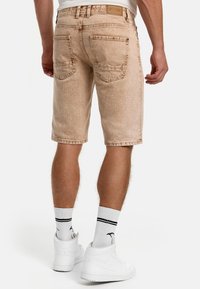 Lys beige denimshorts med en let slidt tekstur, der har baglommer og et mærke ved linningen, parret med hvide højhælede sneakers.