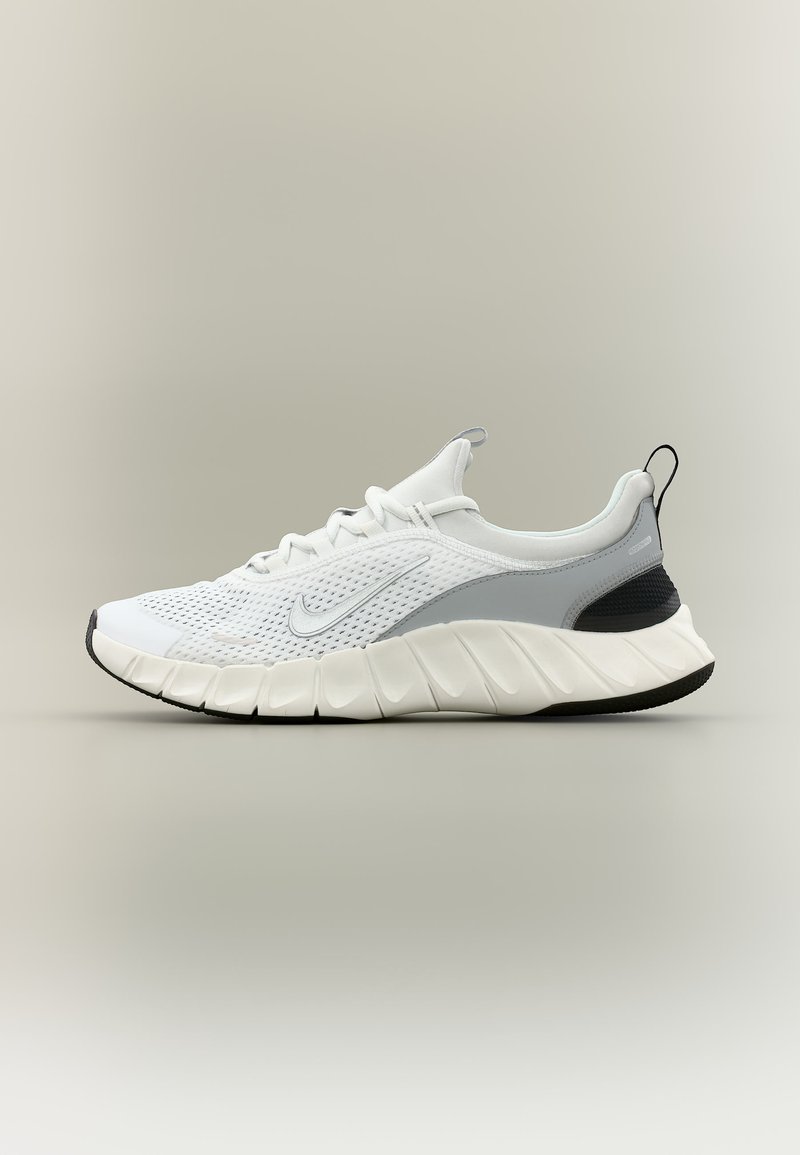 Λευκό και γκρι παπούτσι για τρέξιμο Nike με άνω μέρος από πλέγμα, παχύ μαξιλαρωμένο πέλμα και μαύρη θηλιά στο πίσω μέρος, σε ουδέτερο φόντο.