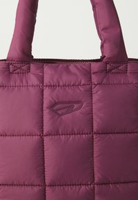 Polstret toteveske i dyp burgunder med et quiltet design, broderte detaljer og en teksturert logo. Har robuste, myke håndtak.